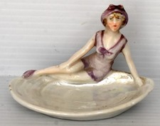 CRESTED CHINA/FAIRGROUND FAIRING: MODEL OF BATHING BELLE LYING ON LUSTRE SHELL 