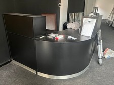Reception Desk In black. Takes up 2meter Sq Area and has storage space Below