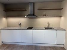 White kitchen units with grey worktop. Hob, fridge, sink and extractor fan