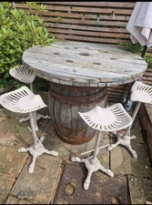 WOODEN BARRELL TABLE AND FOUR CAST IRON TRACTOR SEAT STOOLS - USED IN GARDEN 