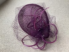 A violet coloured fascinator with a short veil decorated with feathers and beads