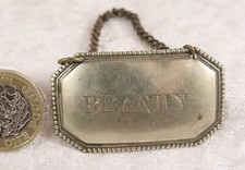 White metal brandy decanter label on a chain 2 inches across drinking home bar