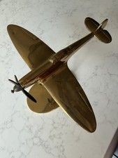 Vintage brass Spitfire-style model plane; one wing needs polish.