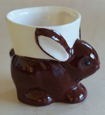 RABBIT EGG CUP - DARK BROWN BUNNY WITH WHITE EARS SEATED WHITE EGG CUP ON BACK 