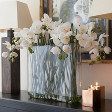 Everlasting artificial faux orchid flower arrangement in a glass vase with resin