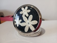 Silver colour double mirror compact black background with three daisies to the f